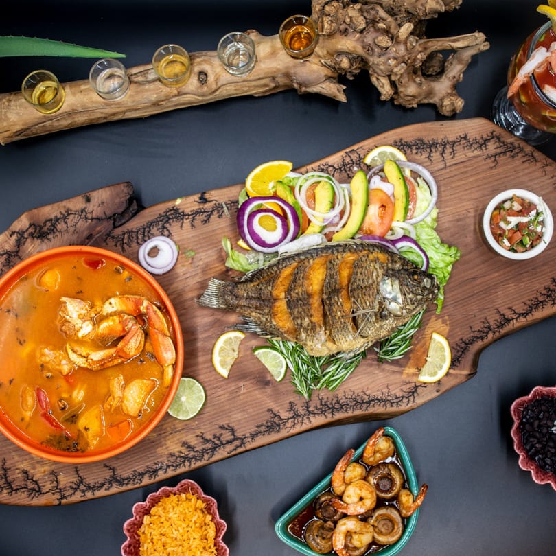 A vibrant spread of Mexican seafood dishes, including whole fried fish, crab soup, and shrimp.