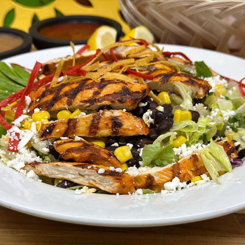 Grilled chicken salad with corn, black beans, cheese, and tortilla strips on a white plate.