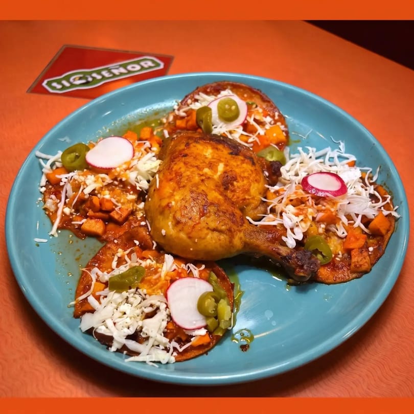 Roasted chicken leg and thigh on a bed of chilaquiles with radish, jalapeños, and cheese.
