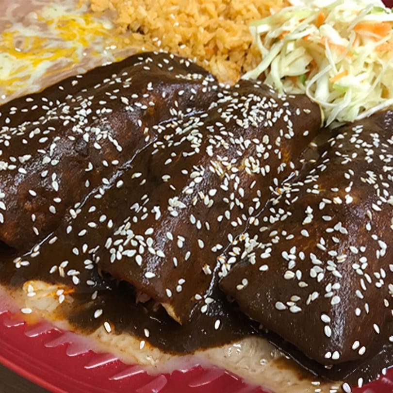 Three mole enchiladas topped with sesame seeds, served with rice, refried beans, and shredded cabbage.