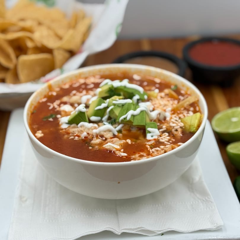 A bowl of tortilla soup with avocado, sour cream, and tortilla strips, with chips and salsa.