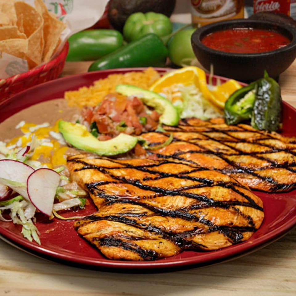 Grilled chicken with rice, beans, avocado, pico de gallo, and radishes on a red plate.