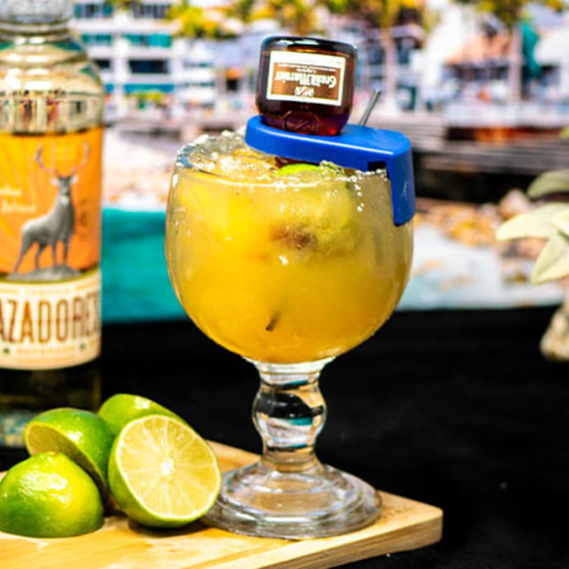 Margarita with a mini Grand Marnier bottle, limes, and a Cazadores tequila bottle on a wooden board.
