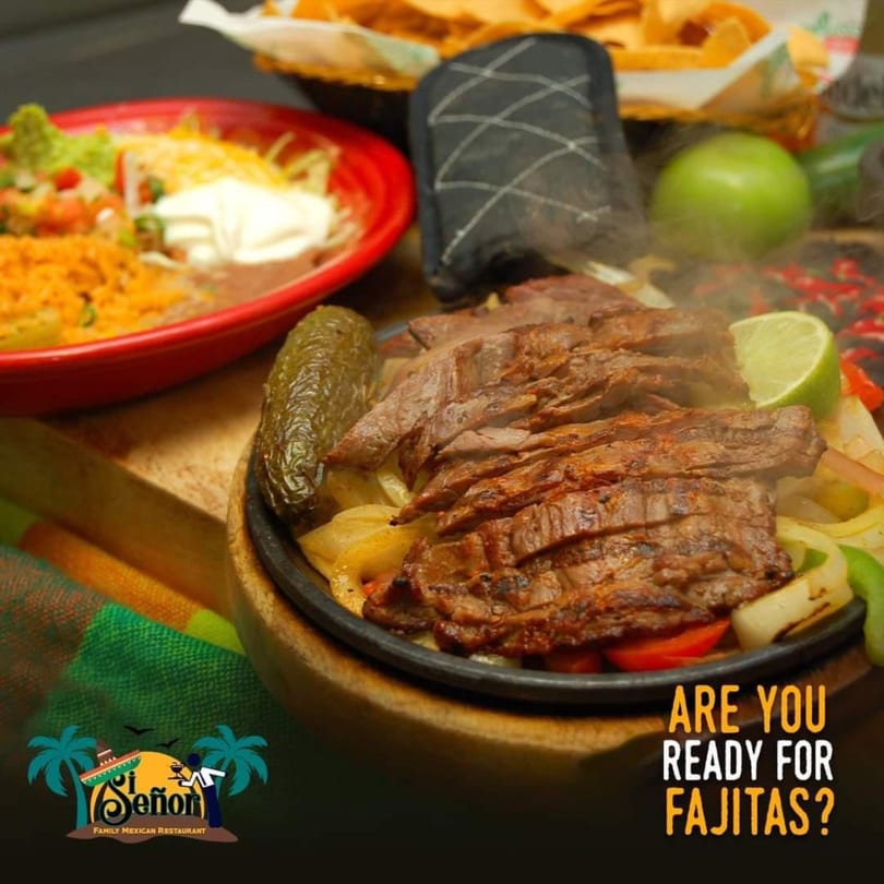 Sizzling steak fajitas with onions, peppers, and a side of rice, beans, and guacamole.