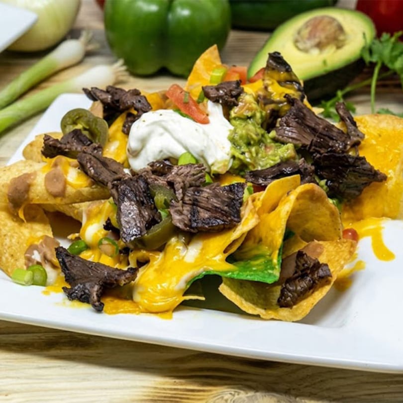 Loaded nachos with steak, cheese, guacamole, sour cream, and jalapeños on a white plate.