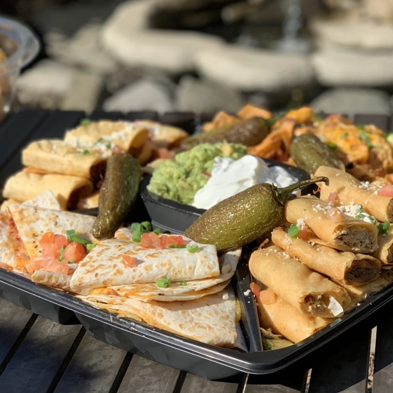 A black platter filled with quesadillas, taquitos, roasted peppers, guacamole, and sour cream.
