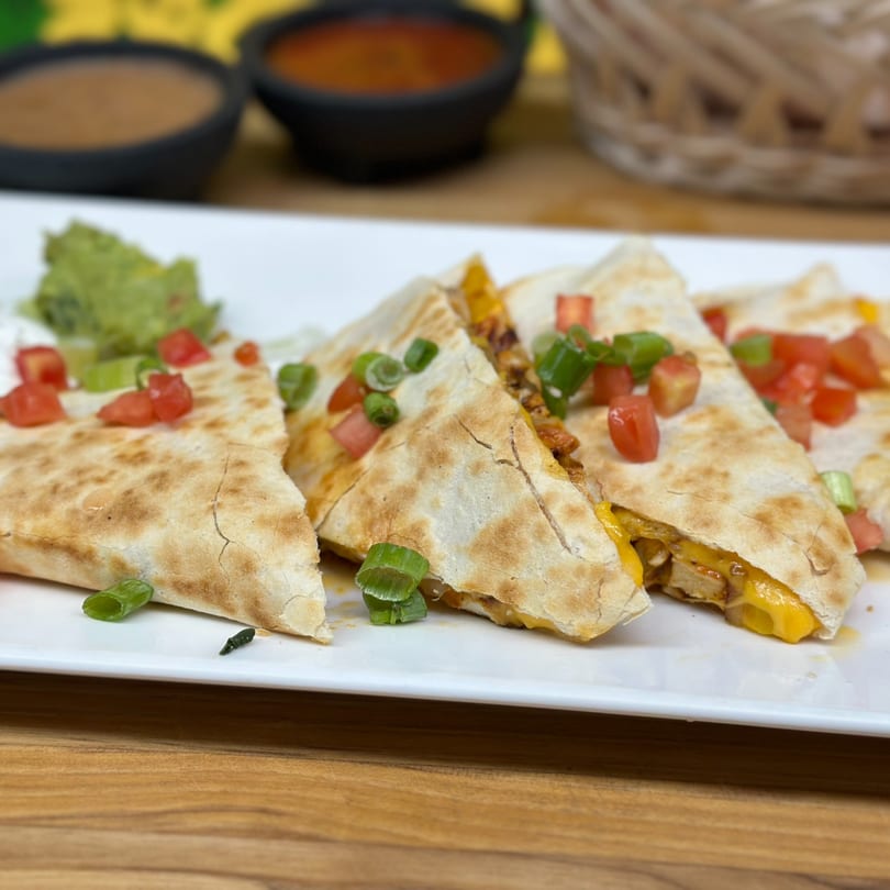 Golden-brown quesadillas filled with cheese and chicken, topped with diced tomatoes and green onions.
