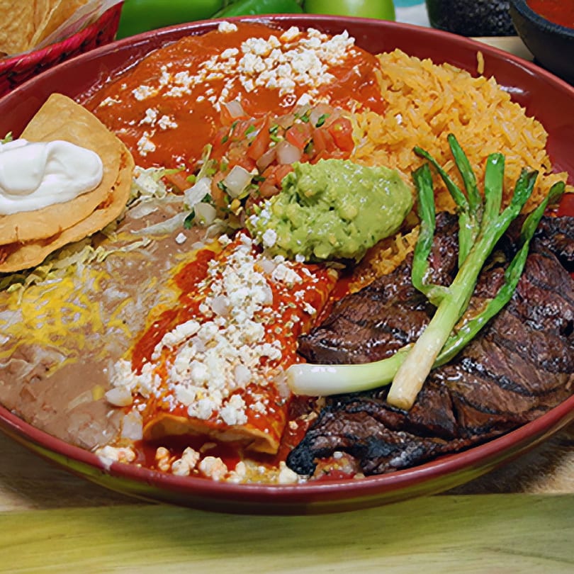 A large red plate filled with various Mexican dishes, including steak, rice, beans, and enchiladas.