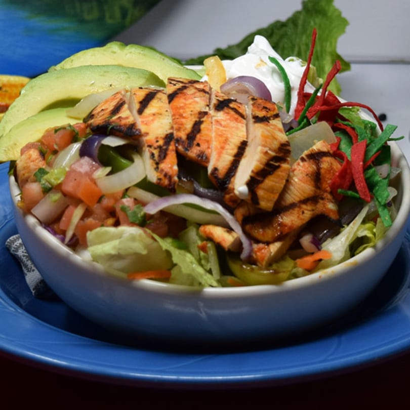 Grilled chicken salad with avocado, pico de gallo, onions, and sour cream in a white bowl.