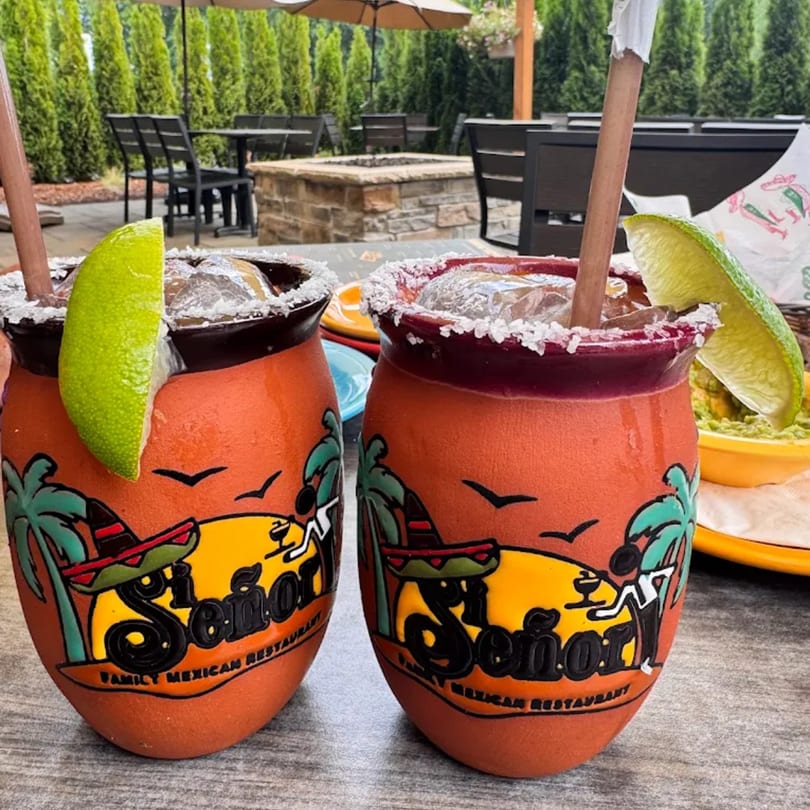 Two Si Señor! margaritas with lime wedges and salted rims on an outdoor patio table.