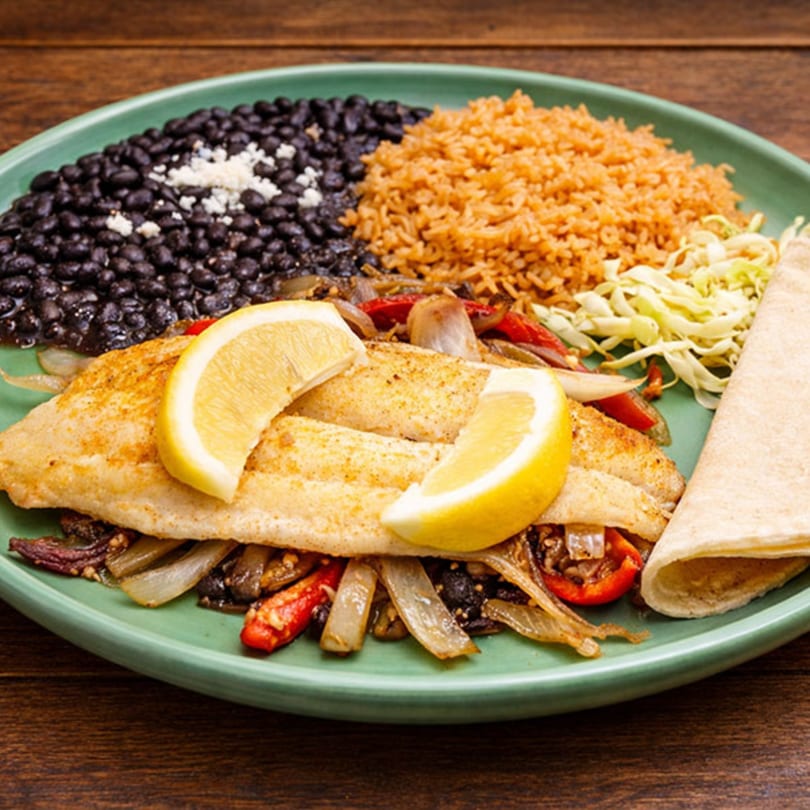 Grilled fish fillets with lemon, black beans, rice, and tortillas on a green plate.