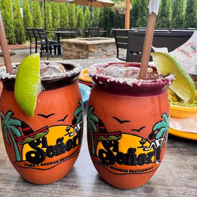 Two Si Señor! margaritas with lime wedges and salted rims on an outdoor patio table.