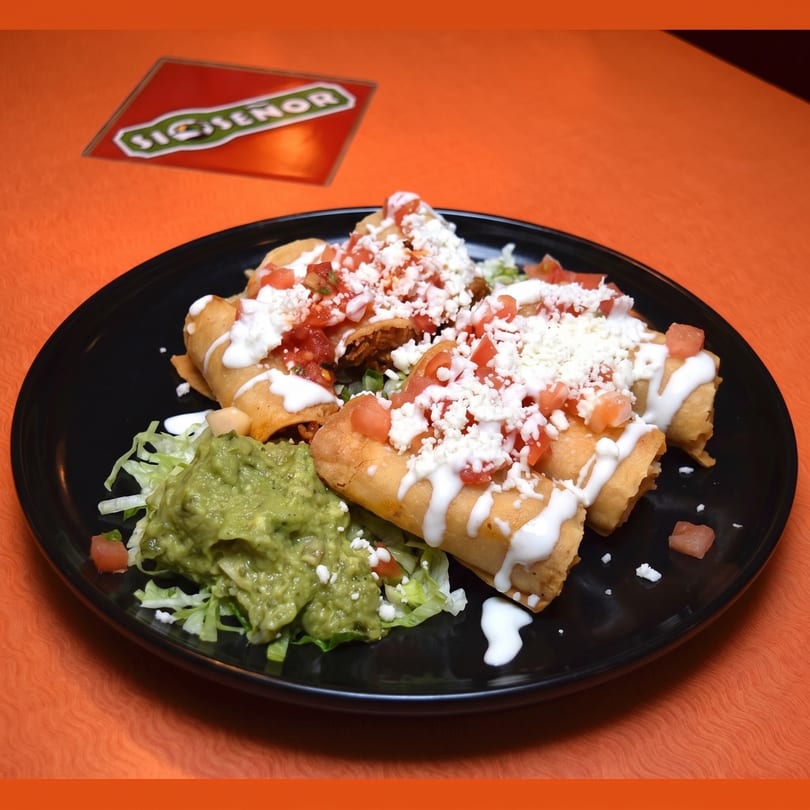 Crispy taquitos topped with sour cream, crumbled cheese, salsa, and a side of guacamole.